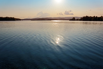 Landscape with water at sunset. Calm summer evening view of Sungul lake in Russia. Beautiful and tranquility scenic scenery of a lake or river with reflection of sun glare.