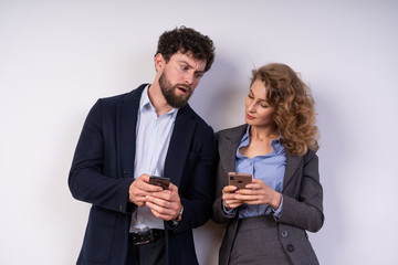 woman and man in suits, business, in a relaxed state, looking at their smartphones.