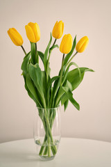 Yellow tulips flowers in a glass vase stand on a white table