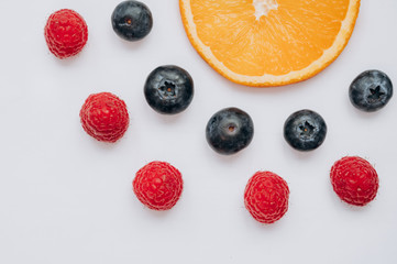 juicy fresh berries blueberries and raspberries lie on a white table next to a slice of orange