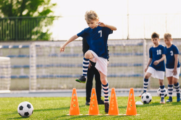 Boy jumping over soccer cones on football training field. Kids on sports training with junior coach. Children on physical education class. Boys imporoving soccer skills