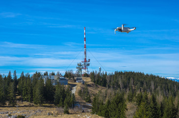 White drone with photo camera flying in the blue sky and telecommunication tower in the background