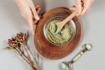 Close up of woman's hands in white shirt mixing organic ubtan with a spoon in wooden bowl. Traditional natural herbal cosmetic agent for skin and hair care handmade creation.