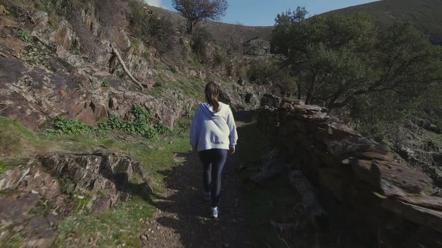 Movin shot of a girl hiking in a rocky path. Beautiful green scenery in Drave, Portugal.