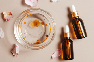 Flat lay of organic beauty face oil serum bottles for cosmetic treatment skin care, bowl of water with oil and flower petals on soft pastel background.