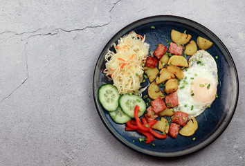 Fried egg with potatoes and ham on a round plate on a light gray background. Top view, flat lay