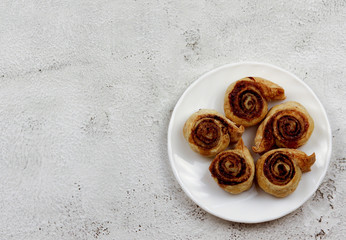 Puff pastry cinnamon rolls on a white round plate on a light gray background. Top view, flat lay