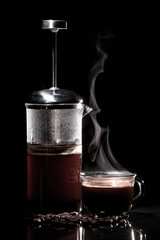 Coffee in a frenchpress on a glass table next to a glass mug