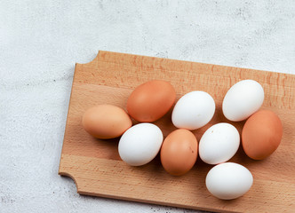 Raw brown and white chicken eggs on a wooden cutting board on a light gray background. Top view, flat lay