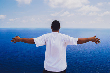 Man raising his hands or open arms standing back looking to sea blue sky horizon