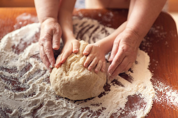 Female and children's hands holding a piece of dough. Female and children's hands knead the dough. Family weekend.