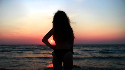 A curly girl standing in front of a sunset at the sea