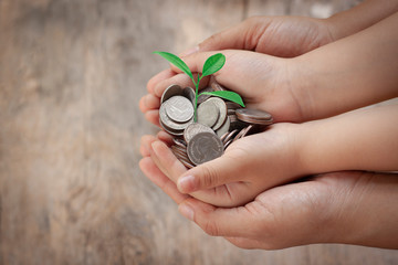 Child and adult hand holding money with green tree. Save money, family finance plan concept to buy house, economy, money in the future and education for thier child on wooden background