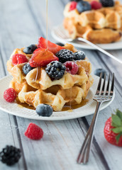A close up of a stack of Belgian waffles topped with berries, powdered sugar and syrup, ready for eating.