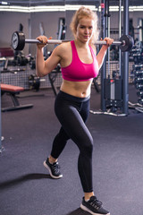 Beautiful brunette woman makes lunges with a barbell in the gym.