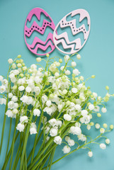 Floral blue background with fresh flowers. Spring greeting card for Easter. A bouquet of lily of the valley and a gift, eggs