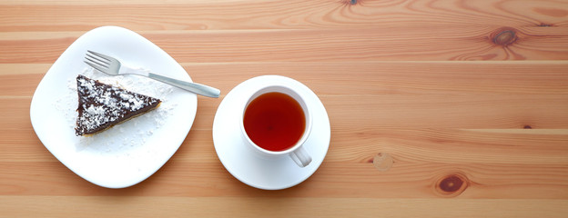 Cup of tea and a slice of chocolate cake on a wooden table. Suitable for advertising background. Food