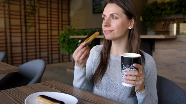 Woman eating chocolate eclair and drinking coffee in a cafe