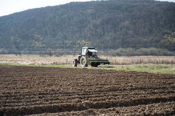 Obraz premium Farmer in tractor preparing land with seedbed cultivator in early spring