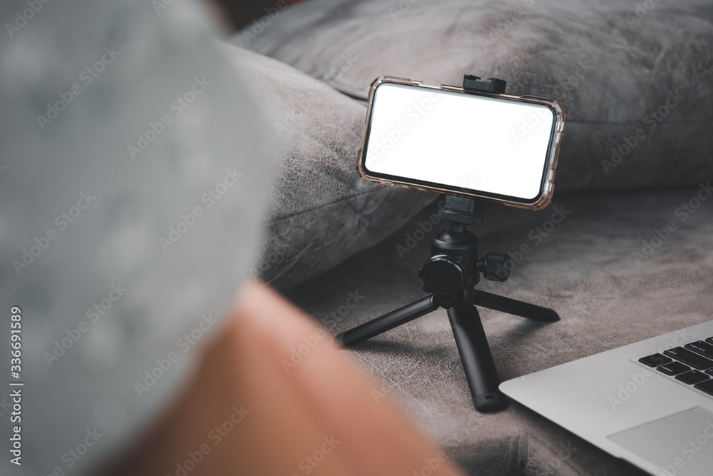 Poster a smartphone with blank screen on tripod.on the sofa