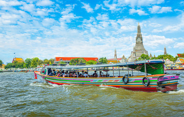 Naklejka premium View over river Chao Phraya from boat back to temple Wat Arun, eldest temple in Bangkok. In foreground is speed longboat passing. Behind are tour boats and ferries. 