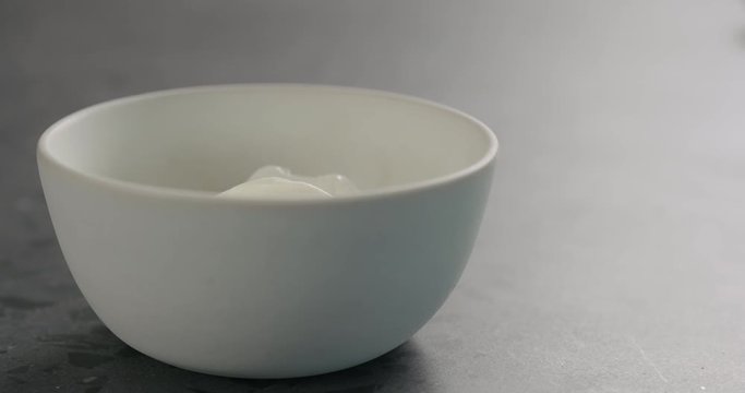 Slow motion pour white yogurt in white bowl on concrete surface