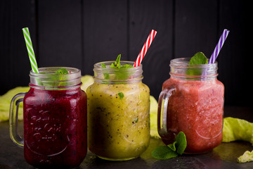 Fototapeta na wymiar three Freshly blended fruit smoothie in glass jar with straw on a dark wood background, Healthy fruit and vegetable smoothies, detox berry drinks, Healthy food for breakfast and snack