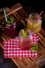 three Freshly blended fruit smoothie in glass jar with straw on a dark wood background, Healthy fruit and vegetable smoothies, detox berry drinks, Healthy food for breakfast and snack