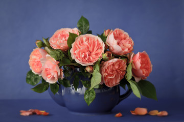 Bouquet of big orange rose flowers in a teapot, blue background, vintage filter effect