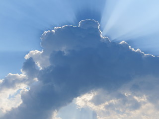 sun rays behind a cloud in a blue sky