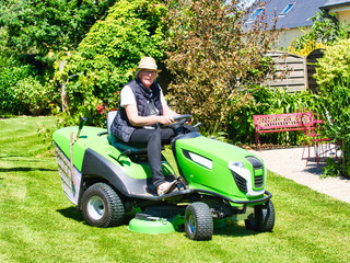 Senior man driving a tractor lawn mower in garden with flowers
