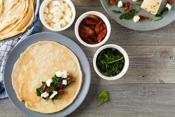 Pancakes with spinach, feta and dried tomatoes. Served on a gray plate. Wooden natural background.