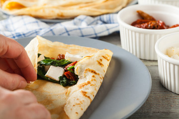 Pancakes with spinach, feta and dried tomatoes. Served on a gray plate. Wooden natural background.
