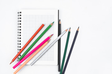 Some different color wood pencil crayons scattered across and on top of a white diary