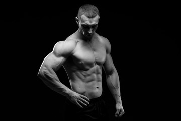 Fototapeta premium Muscular model sports young man in jeans showing his press on a black background. Fashion portrait of sporty healthy strong muscle guy. Sexy torso. Black and white photography 