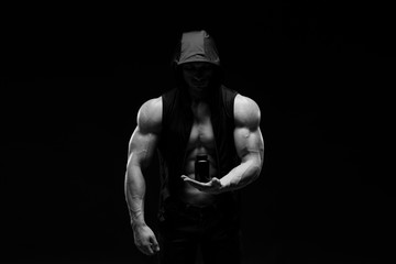 Fototapeta na wymiar Muscular bodybuilder with jar of protein on a dark background. Sports nutrition. Bodybuilding nutrition supplements, sport, workout, healthy lifestyle concept. Black and white photography