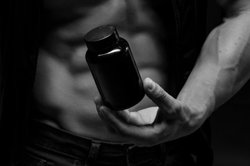 Muscular bodybuilder with jar of protein on a dark background. Sports nutrition. Bodybuilding nutrition supplements, sport, workout, healthy lifestyle concept.  Black and white photography