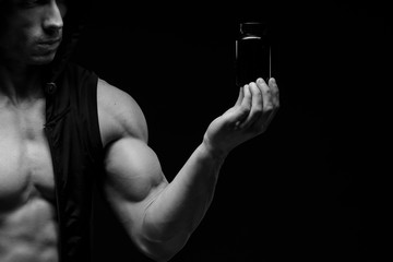 Muscular bodybuilder with jar of protein on a dark background. Sports nutrition. Bodybuilding nutrition supplements, sport, workout, healthy lifestyle concept.  Black and white photography