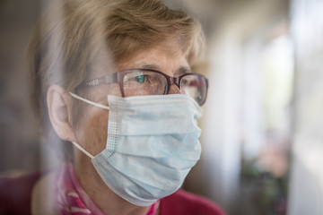 Seniorin mit Mundschutz schaut aus dem Fenster