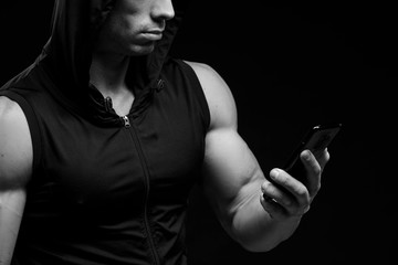Muscular bodybuilder with phone in hands on a dark background. Sports nutrition. Bodybuilding nutrition supplements, sport, workout, healthy lifestyle concept.