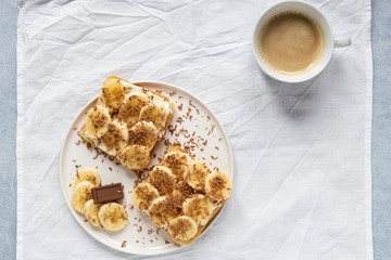 french toast with banana and chocolate on white plate and coffee gray background top view flat lay