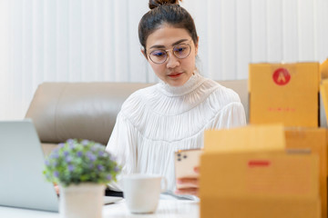 Fototapeta na wymiar Asian woman working from home. Young Asian woman freelance start up small business owner using smartphone for check her order, email from customer in her home. Concept of Online selling, e-commerce.