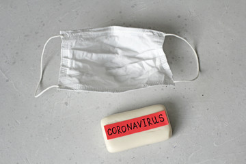 Protective medical hygiene mask, soap lie on light background, word coronavirus is written on soap....