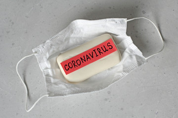 Protective medical hygiene mask, soap lie on light background, word coronavirus is written on soap....