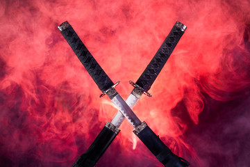 Partially drawn blades of two katanas in red smoke