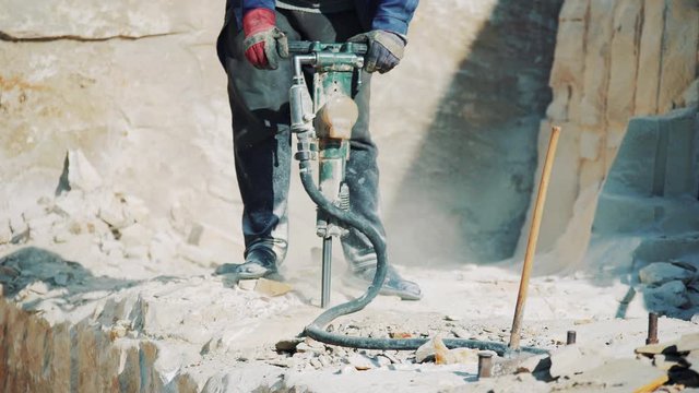 A worker at a stone quarry drills a sandstone block with a jackhammer. Stone mining industry.
