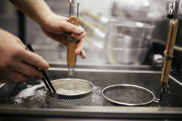 Male's hands cooking boiling asian style egg noodles for ramen in pot in strainers, horizontal