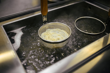 Cooking boiling asian style egg noodles for ramen in pot in strainers, horizontal