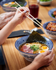 Female with chopsticks eating asian japanese shio ramen noodle soup with eggs, pastrami and spinach, vertical