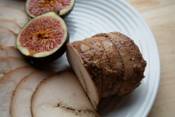 On a white plate meat roll with chopped ripe figs. The roll is cut into round pieces